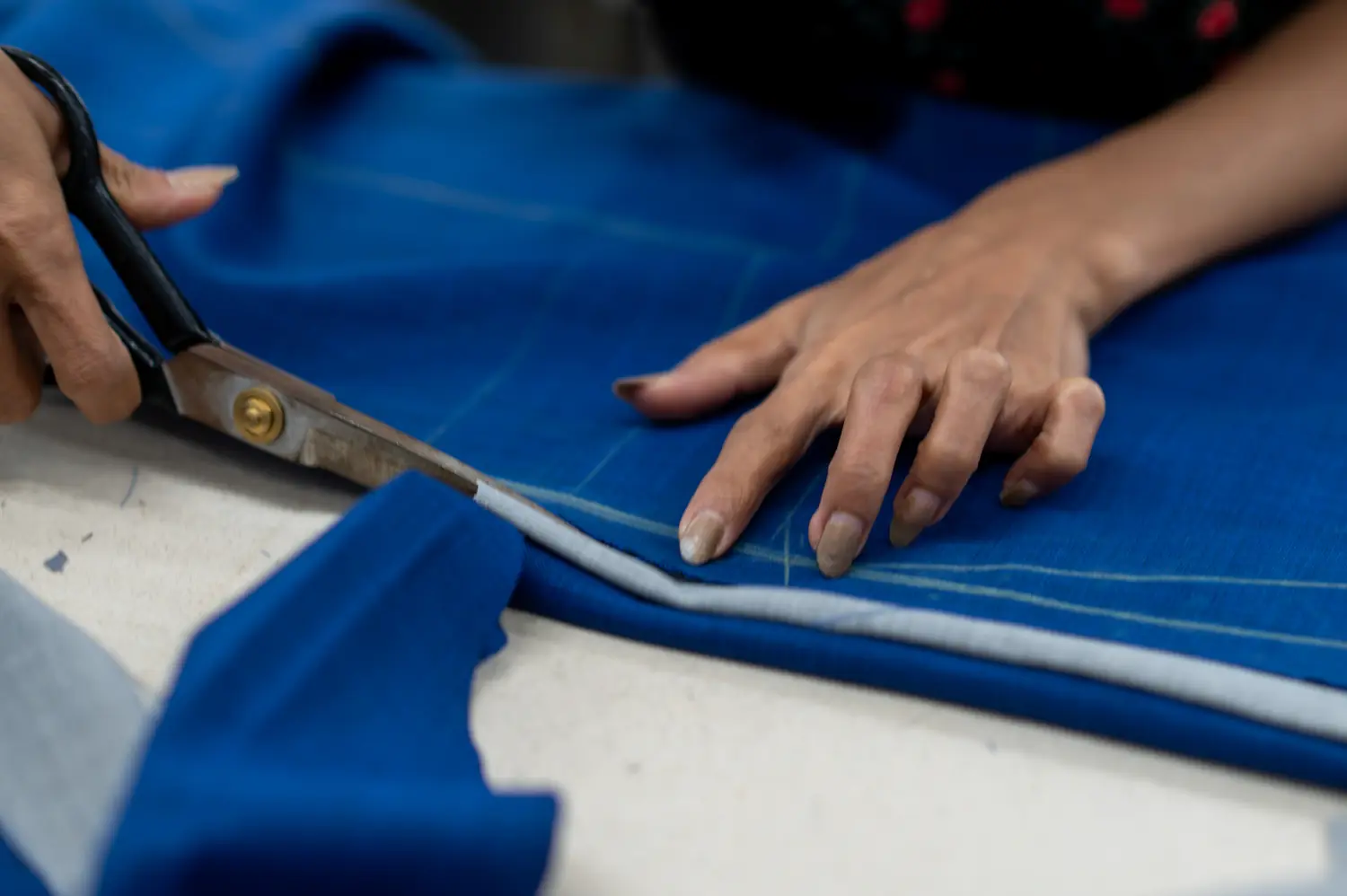 Tailor cutting blue fabric by hand in the Sawasdee workshop